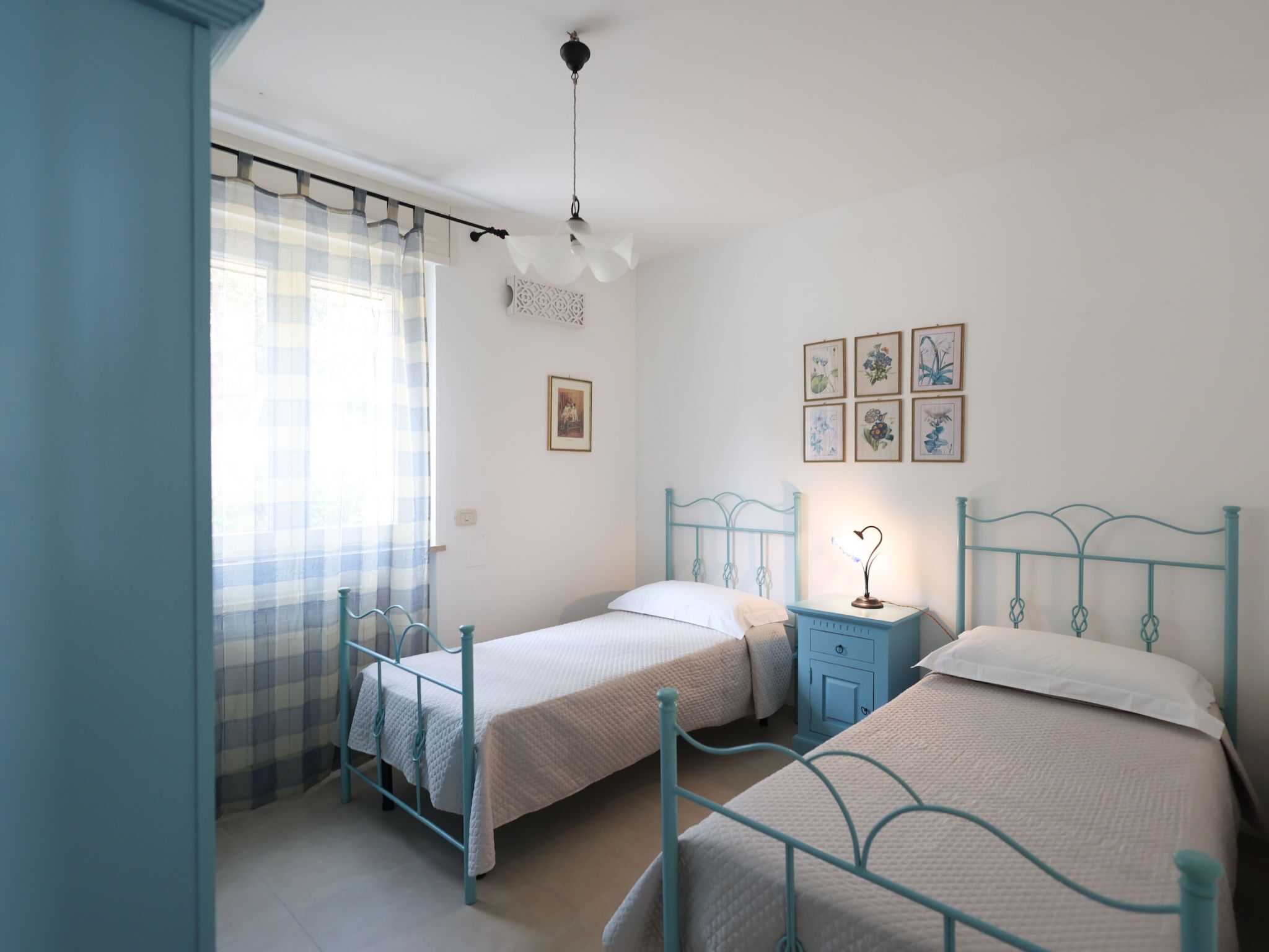 Une chambre avec deux lits, une table de chevet, un ventilateur de plafond et une fenêtre avec des rideaux.