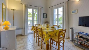 Un comedor con una mesa dispuesta para cuatro personas, un televisor montado en la pared y una estantería llena de libros.
