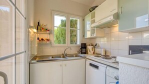 Cocina compacta con armarios blancos, lavavajillas, cafetera y ventana con vistas a zonas verdes.