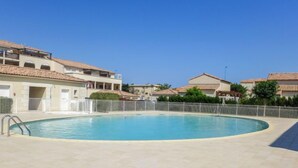 Una piscina con borde de baldosas, rodeada por una valla blanca y edificios residenciales con balcones.