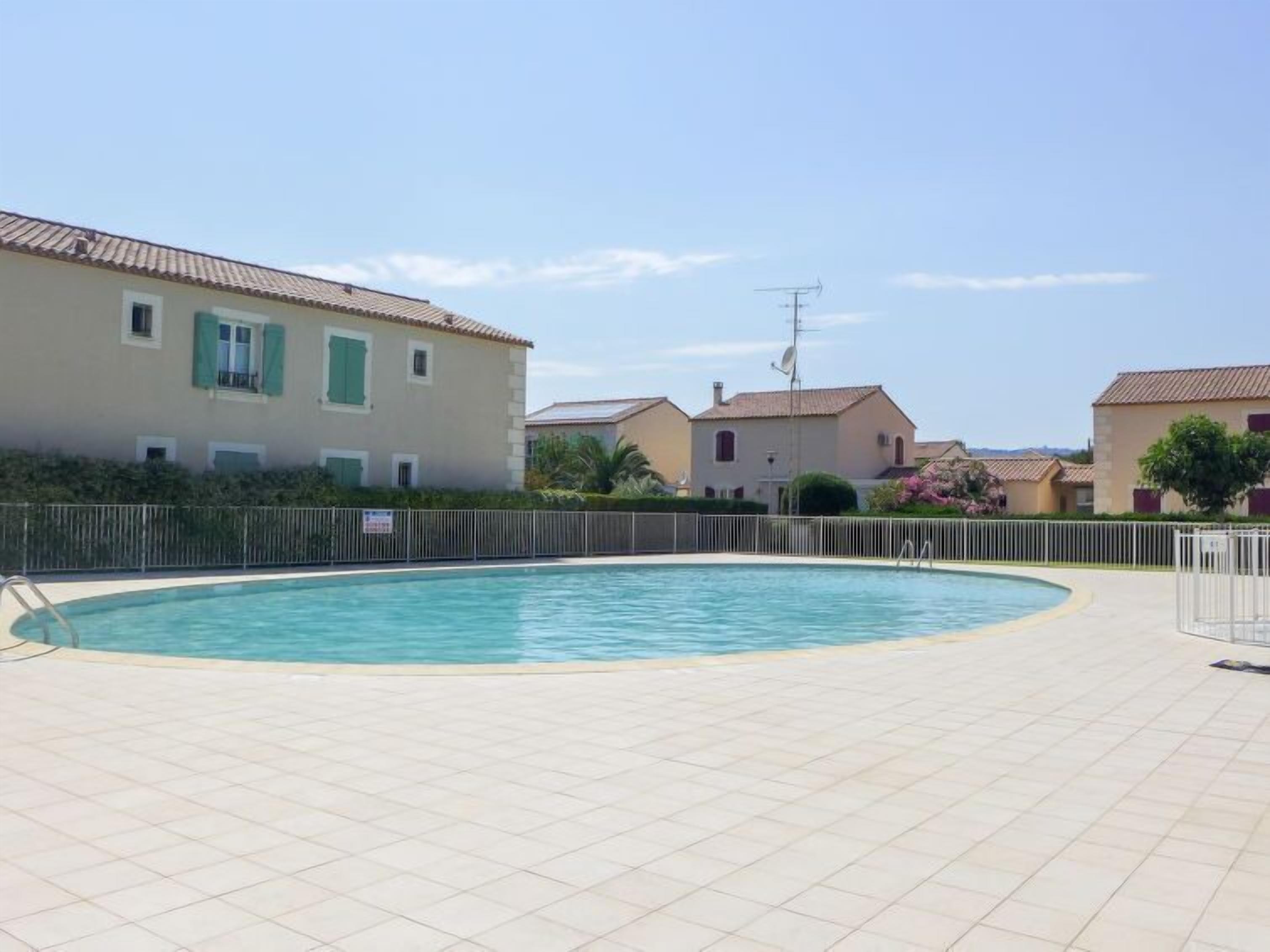 A swimming pool with a tiled deck, surrounded by buildings with Mediterranean architecture.