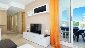 Ein modernes Wohnzimmer mit Flachbildfernseher, weißem Unterhaltungsschrank und einer Glasschiebetür zum Essbereich im Freien.
