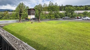 Une zone herbeuse avec une terrasse en bois, un petit bâtiment et un parking avec des voitures.