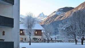 Un paysage enneigé avec un bâtiment doté d’une façade en bois et une chaîne de montagnes en arrière-plan.
