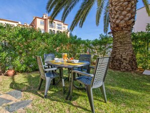 A patio with a round table and chairs, surrounded by lush greenery and a palm tree.