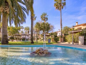 A pool with clear water, surrounded by palm trees and a gazebo.