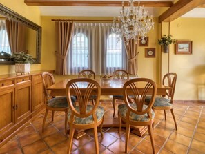 A dining room with a wooden table, six chairs, a chandelier, and a large mirror.