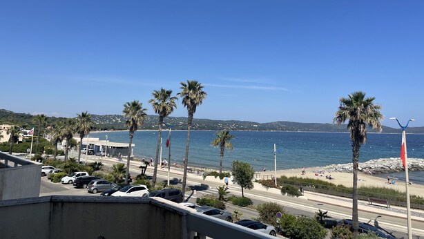Eine Küstenstraße mit parkenden Autos, Palmen und einem Strand im Hintergrund.