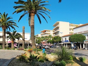 A street with palm trees, a café, and a building with a sign that reads "MAILLOT DE BAIN".
