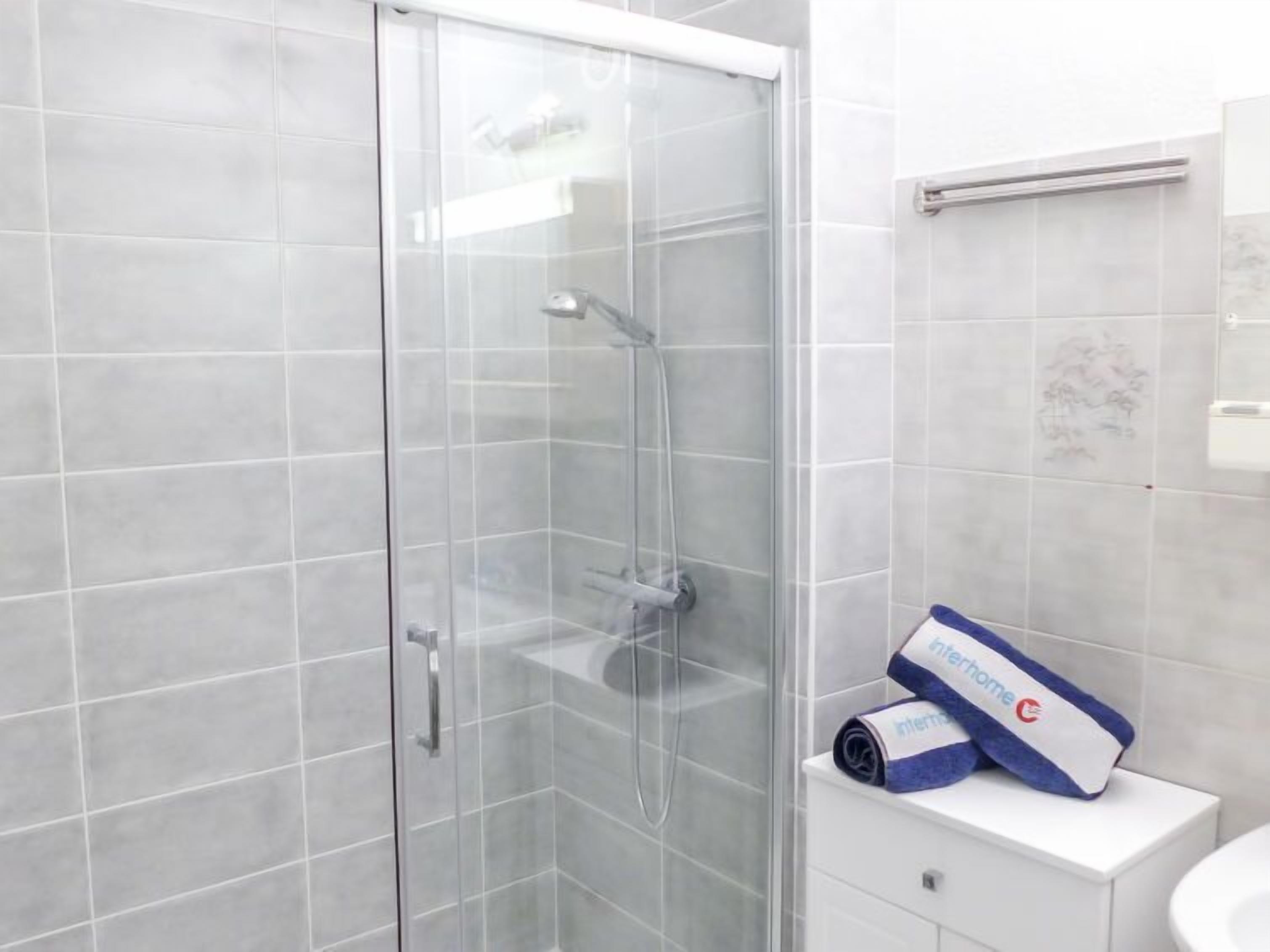 A modern bathroom with a glass-enclosed shower, a white sink, and a towel with a logo on the counter.