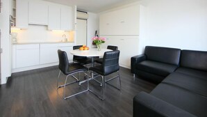 Een moderne woonkamer met een zwarte leren bank, een eettafel met vier stoelen, en een keuken met witte kasten.