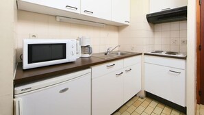 A compact kitchen with white cabinets, a microwave, a coffee maker, and a stove. - Astrid 702 with parking by Interhome (Bredene)