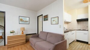 A small, modern room with a sofa, a wooden dresser, and a kitchenette. - Astrid 702 with parking by Interhome (Bredene)