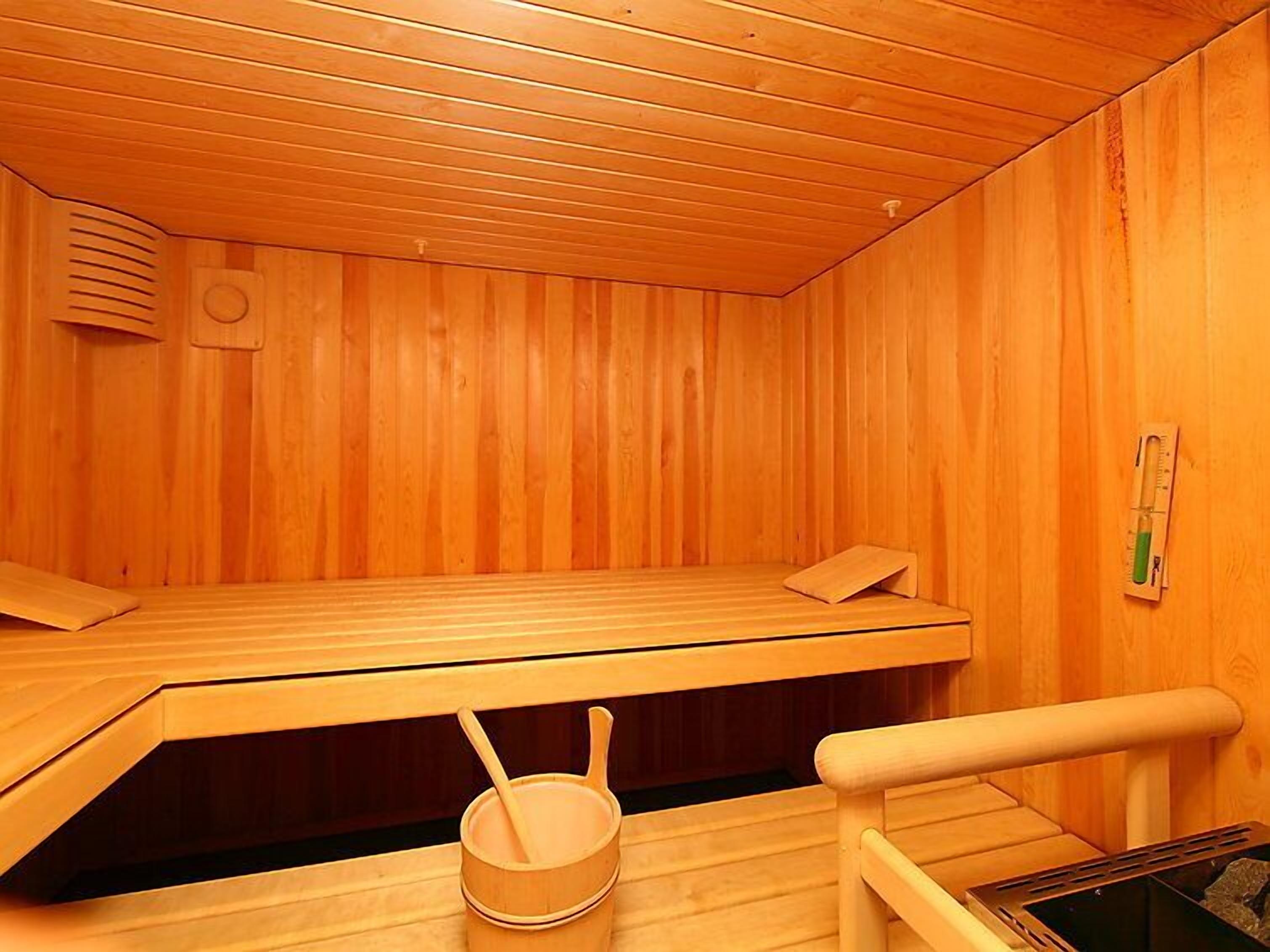 A wooden sauna room with benches, a wooden bucket, and a thermometer on the wall.