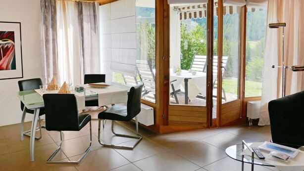 A modern room with a dining table, chairs, and a sliding glass door leading to an outdoor area with a table and chairs.
