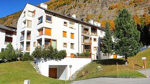 A multi-story building with balconies, a garage, and a view of a mountainous landscape.