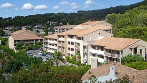 A multi-story hotel with a central courtyard, surrounded by lush greenery and a hilly backdrop.