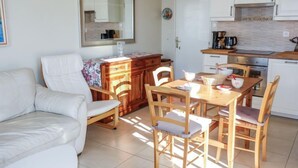 A compact living space with a sofa, wooden dining table, chairs, a kitchen area with cabinets and appliances, and a large mirror.