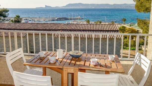 A wooden table with white chairs on a balcony overlooking the sea.