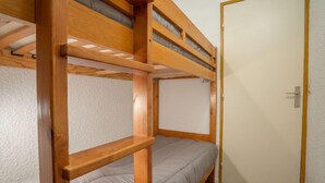 Ein Schlafraum mit Etagenbetten, einem Holzbettgestell, einer Tür und einer Wand mit strukturierter Oberfläche.