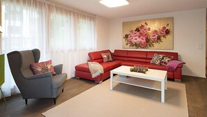 A living room with a red sofa, a grey armchair, a white coffee table, and a large floral painting on the wall.