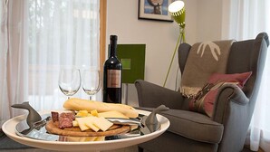 A dining table with a charcuterie board, wine glasses, and a bottle of wine in a living room with a sofa and a lamp.