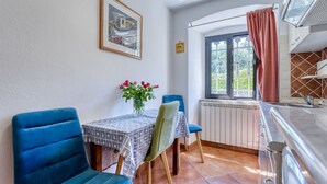 A dining area with blue chairs, a table with a patterned tablecloth, a vase with flowers, and a window with a view of greenery. - Lovrano by Interhome (Lovran)