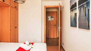 A hotel room with a bed, a wooden wardrobe, a door leading to another room, and a wall-mounted artwork.