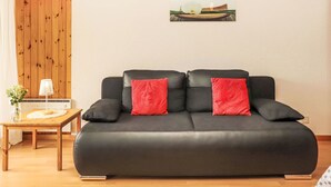 A black leather sofa with red cushions, a small wooden table with a lamp and vase, and a framed picture on the wall.