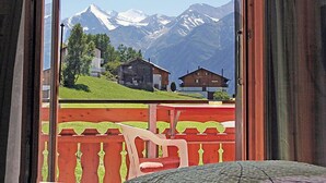 Ein Zimmer mit Blick auf schneebedeckte Berge, einer Holzdachterrasse und einem roten Geländer.