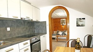 Eine kompakte Küche mit modernen Geräten, ein Essbereich mit Holztisch und ein gemütlicher Wohnbereich, der durch einen Bogen sichtbar ist.