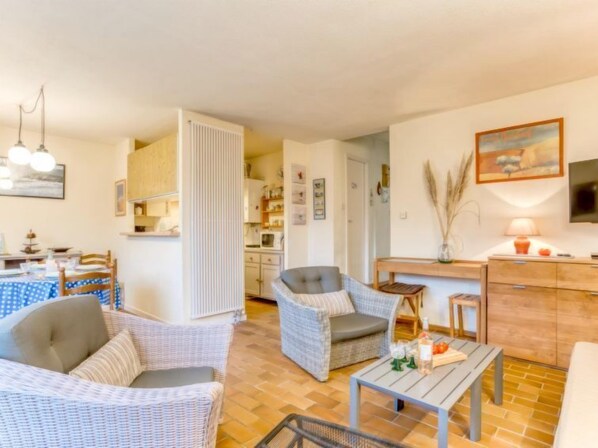 Una sala de estar acogedora con muebles de mimbre, un comedor con mantel azul y una cocina al fondo.