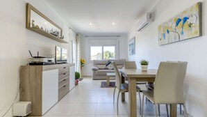 A modern living room with a sofa, dining table, and chairs. There is a TV on a wooden cabinet, and a painting on the wall. - El Santiago II by Interhome (Roses)