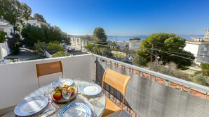 A balcony with a table set for two, overlooking a coastal town with buildings and trees. - El Santiago II by Interhome (Roses)