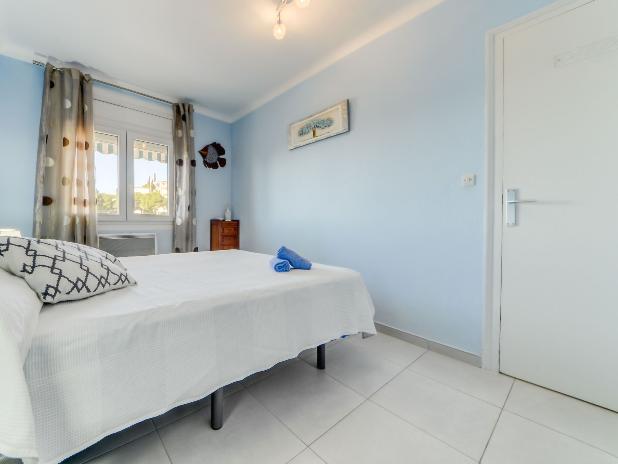 Een slaapkamer met een bed, een kaptafel, een raam met gordijnen en een deur.
