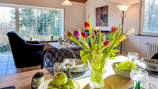 A dining area with a table set for two, featuring a vase of tulips, a bowl of green apples, and various glassware. - Wanderlust by Interhome (Dittishausen)