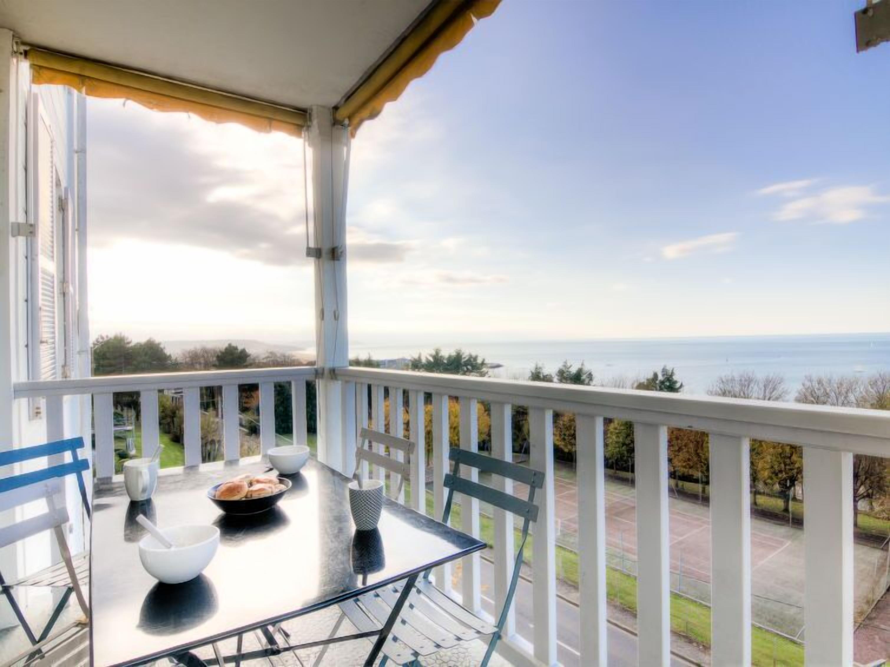 Un balcon avec une table dressée pour le petit-déjeuner, offrant une vue panoramique sur la mer et le paysage lointain.