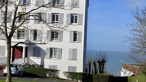 Um edifício de vários andares com paredes brancas e portões, uma porta vermelha e vista para o mar.