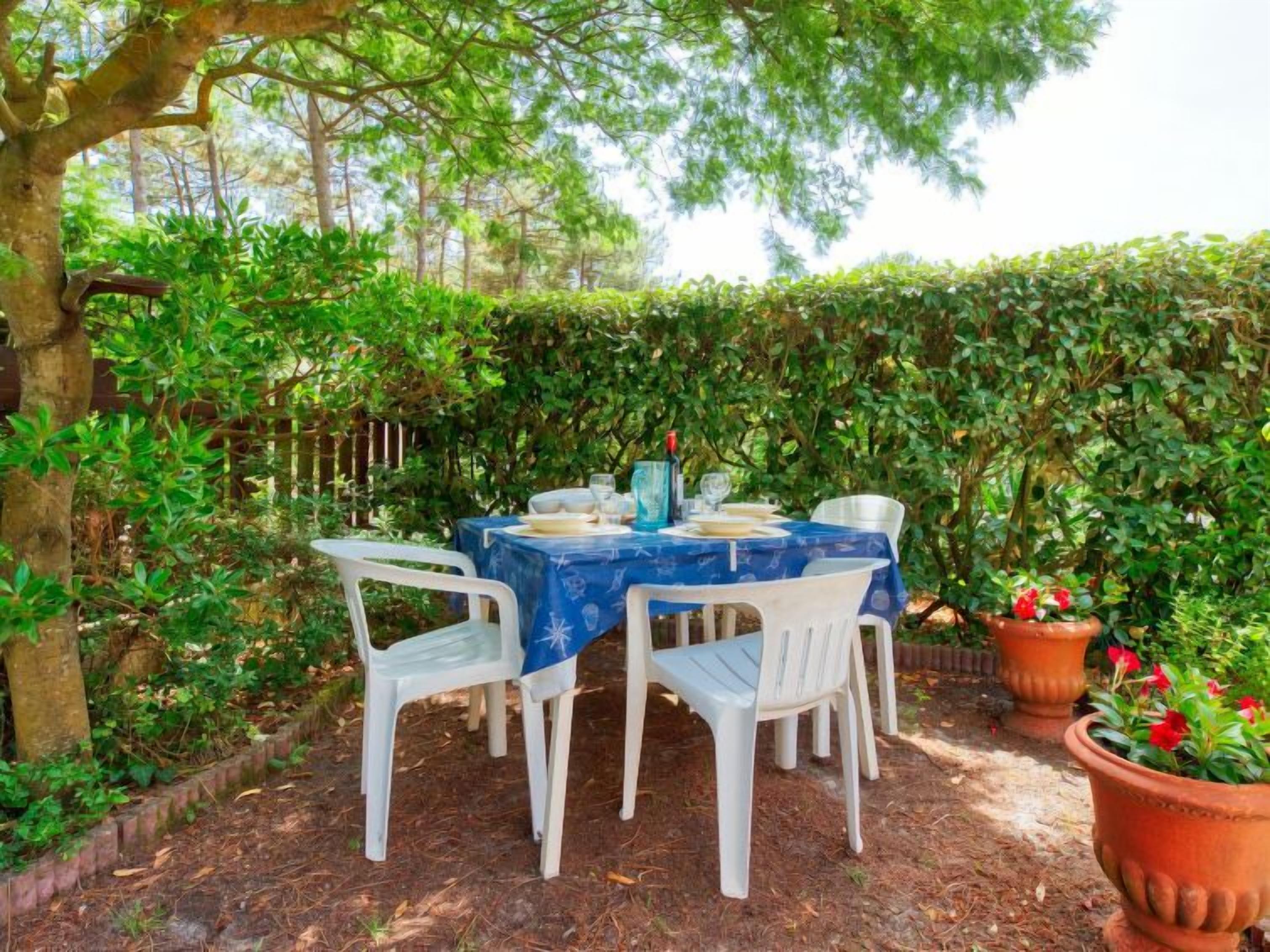 An outdoor dining area with a table set for four, surrounded by lush greenery and a hedge.