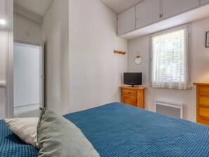 A bedroom with a bed, a television on a wooden cabinet, a window with curtains, and a door. - Les Palombes by Interhome (Lacanau)