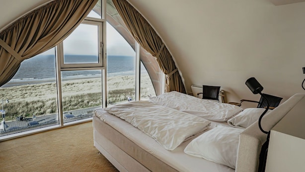 Une chambre avec une grande fenêtre donnant sur la plage et l’océan.