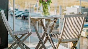 Un balcon avec une table et deux chaises, un vase rempli de fleurs et une vue sur la mer et la plage.
