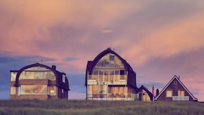 Une maison moderne dotée d’une grande façade en verre, d’une petite structure attenante et d’une maison traditionnelle avec une cheminée.