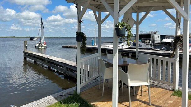 A gazebo with a table and chairs, overlooking a calm body of water with a sailboat in the distance. - Dorregeest by Interhome (Uitgeest)