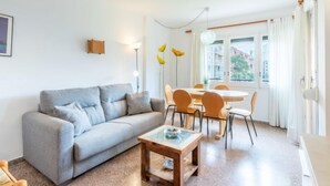 Een woonkamer met een grijze bank, een houten salontafel, en een eetgedeelte met een tafel en stoelen.