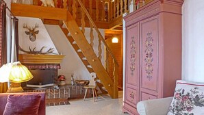 A cozy living room with a fireplace, a staircase, and a pink cabinet. - Apartment Biwak by Interhome (Wengen)