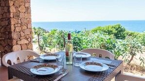 Une table dressée pour deux personnes, avec assiettes, couverts et verres, donnant sur une vue sur la côte.