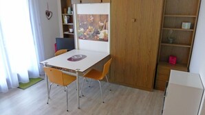 A room with a white table, two yellow chairs, a whiteboard, a bookshelf, and a wooden wardrobe.