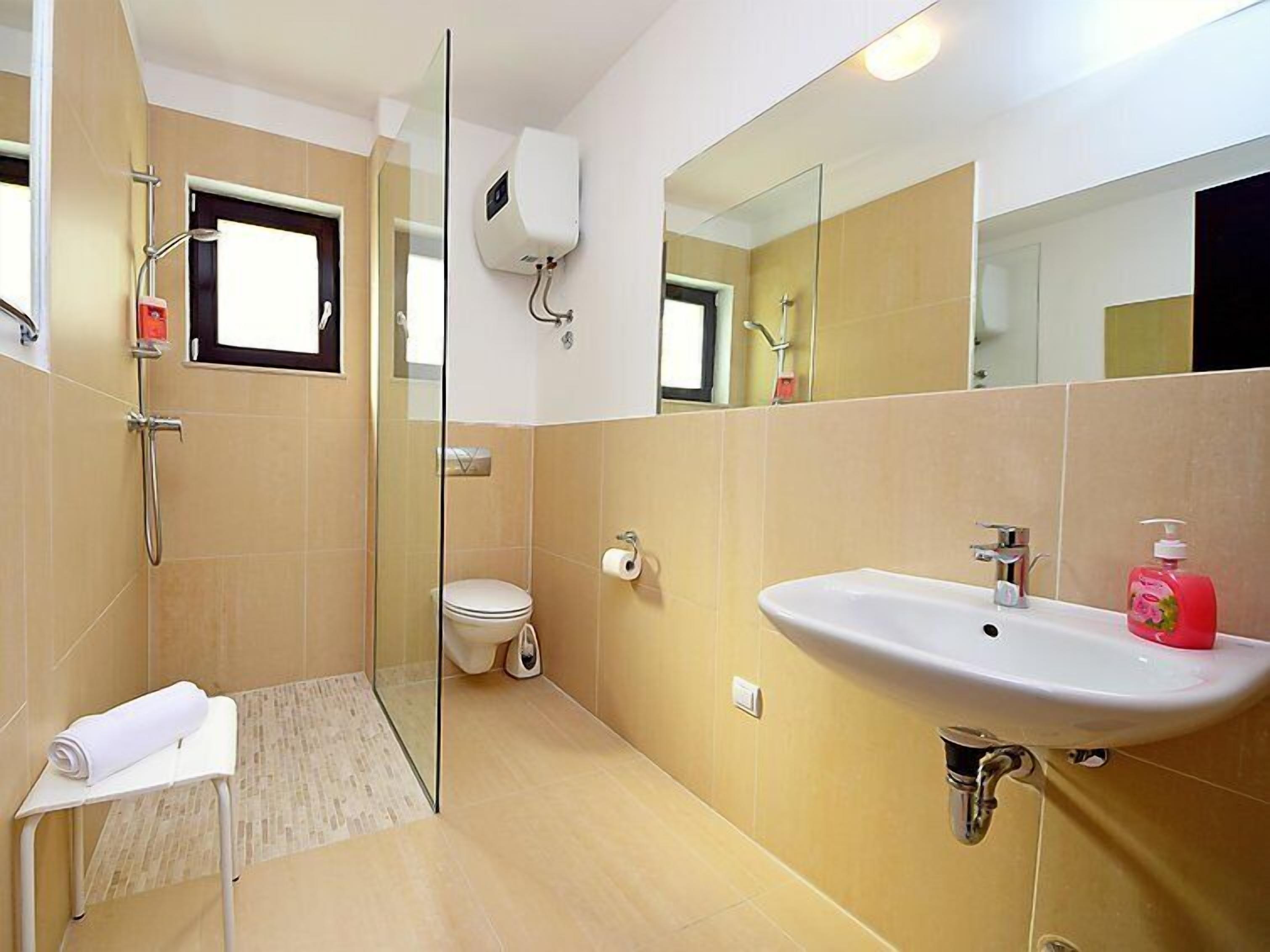 A modern bathroom with a glass shower enclosure, a toilet, a sink with a mirror, and a towel on a small table.