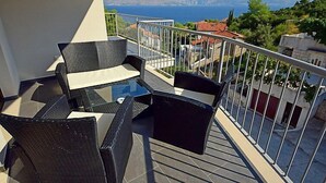 A balcony with wicker furniture and a glass table, overlooking a scenic view of the sea and mountains. - Molo Lozna by Interhome (Brač/Postira)